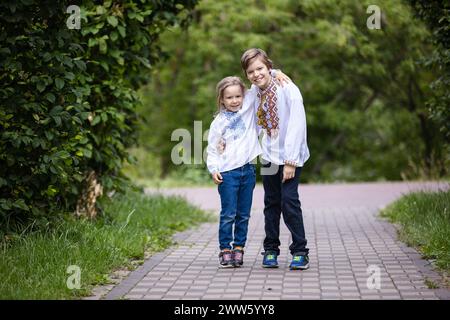 Bambini piccoli che indossano camicie tradizionali ricamate ucraine che si abbracciano mentre guardano la macchina fotografica. Fratello e sorella in posa all'aperto nel parco Foto Stock