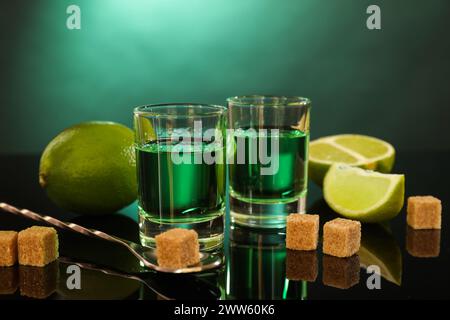 Absinthe in bicchieri da shot, zucchero di canna, lime e cucchiaio sul tavolo a specchio. Bevanda alcolica Foto Stock