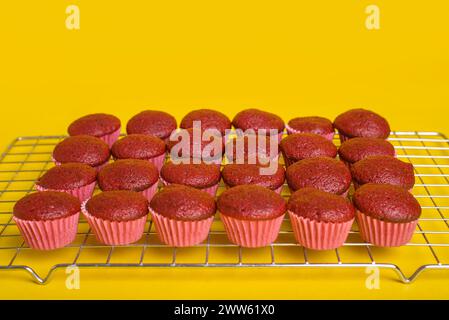 Cupcake di velluto rosso appena sfornati rinfrescanti su sfondo giallo. Foto Stock