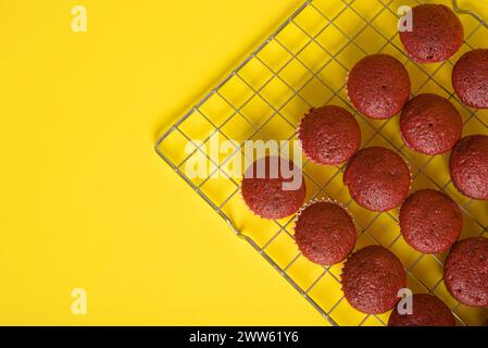 Cupcake di velluto rosso appena sfornati rinfrescanti su sfondo giallo. Foto Stock