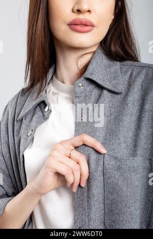 Una giovane donna elegante con una camicia grigia si posa con la mano in tasca, mostrando la moda moderna. Foto Stock