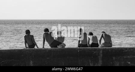 Sei ragazzi seduti su una banchina a Malecón, l'Avana, Cuba. Foto Stock