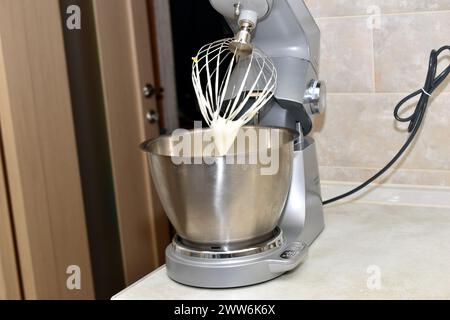 Vista laterale di un mixer da cucina con frusta e recipiente in metallo inossidabile dopo aver preparato la panna. Foto Stock