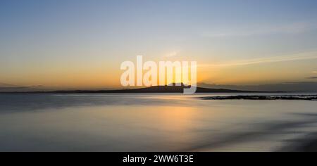 Bagliore dorato in cima all'isola di Rangitoto mentre il sole sorge sopra l'orizzonte. Milford Beach. Auckland. Foto Stock