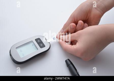 Applicazione del sangue dal dito alla striscia e dispositivo per la misurazione dei livelli di glucosio nel sangue. Concetto di monitoraggio della salute e gestione del diabete Foto Stock