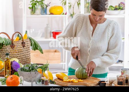 Giovane donna nella sua cucina circondata da verdure biologiche. Foto Stock