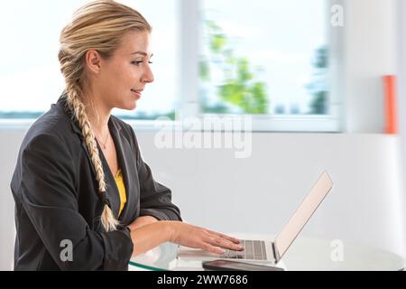 Giovane donna bionda di profilo con le mani sulla tastiera del computer. Foto Stock