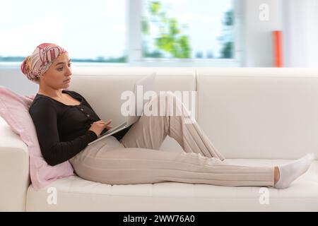 Donna con una sciarpa nei capelli distesa sul divano, un portatile in ginocchio. Foto Stock