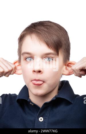 Un ragazzo che indossa una polo blu che tira le orecchie e tira fuori la lingua per creare un volto divertente. Ritratto in studio su sfondo bianco Foto Stock
