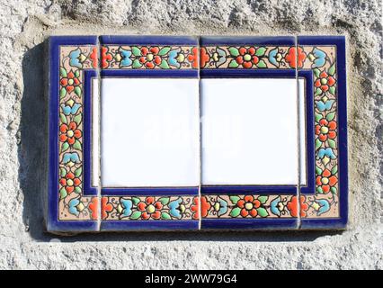 collage, insegne di ceramica in smalto o argilla su un muro rustico in pietra. blu, rosso, fiori gialli, foglie verdi sono disegnate con motivo. lastra di pietra rettangolare Foto Stock