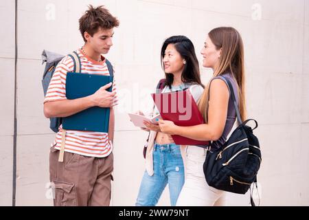 Sorridenti amici di studenti universitari che guardano appunti, parlano e ridono nel campus. Foto Stock