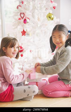 Due giovani ragazze apertura presenta sotto albero di Natale, sorridente Foto Stock