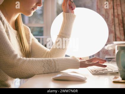 Profilo di donna digitando sulla tastiera del computer contro la Lampada sferica, vista da vicino Foto Stock