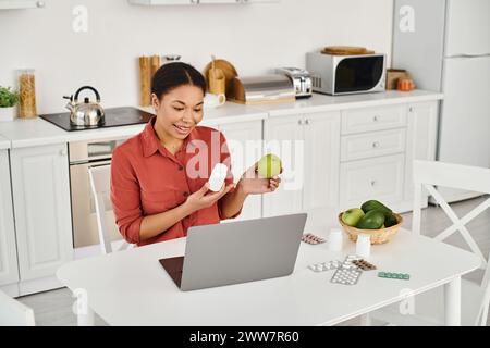 nutrizionista afroamericano che tiene in mano mele e integratori mentre dà consigli sulla dieta online Foto Stock