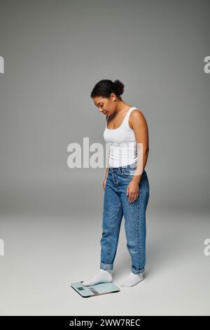 giovane e felice donna afroamericana in un abbigliamento casual in piedi su scale, sfondo grigio Foto Stock