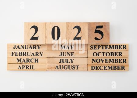 Anno 2025 scritto su cubi di legno sopra i mesi dell'anno scritto su dodici pezzi rettangolari di legno. Isolato su sfondo bianco. Foto Stock