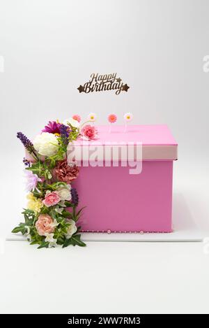 Torta finta o torta regalo in rosa e bianco, decorata con una disposizione floreale isolata su sfondo bianco. Foto Stock