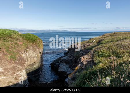 tranquilla scena costiera con scogliere erbose, coste rocciose e un mare calmo sotto un cielo limpido, che evoca tranquillità Foto Stock