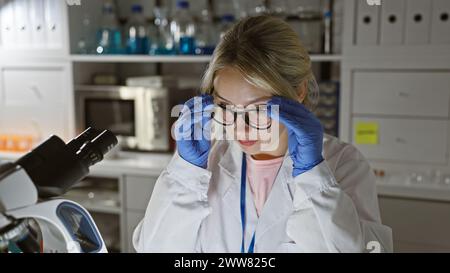 Donna bionda scienziata che regola gli occhiali in laboratorio Foto Stock