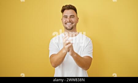 Un allegro giovane ispanico con una barba che batte le mani contro un muro giallo isolato Foto Stock