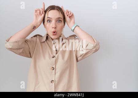 Giovane donna caucasica che indossa una camicia casual che fa un gesto divertente con il dito sopra la testa come corna di toro Foto Stock