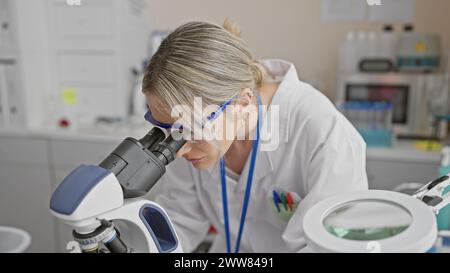 Scienziata bionda che esamina il campione al microscopio in un laboratorio interno Foto Stock