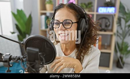 Donna sorridente con cuffie che parla in uno studio radio, ritraendo un'atmosfera da emittente professionale. Foto Stock