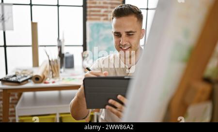 Bel giovane con un tablet digitale sorride mentre lavora in uno studio luminoso e moderno. Foto Stock