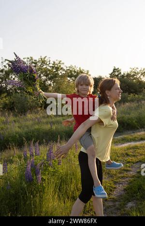 Mamma felice e figlio carino che si coccolano e si abbracciano tra i fiori selvatici in un campo. Foto Stock