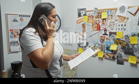 La detective ispanica analizza le prove in un ufficio con una commissione investigativa mentre parla al telefono. Foto Stock