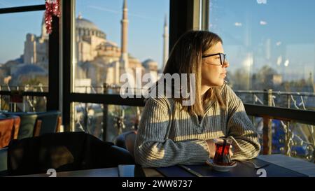 Una donna contemplativa gusta il tè in un ristorante con vista di hagia sophia a istanbul al tramonto. Foto Stock