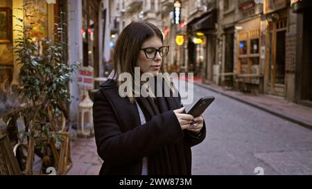 Donna adulta che naviga sullo smartphone nella storica strada di istanbul, mostrando viaggi e vita urbana in turchia. Foto Stock