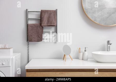 Portasciugamani riscaldato con asciugamani marroni in bagno Foto Stock