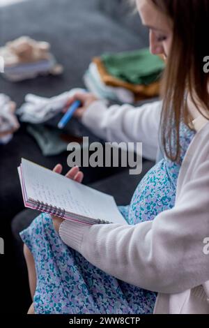 Donna incinta che scrive la lista di imballaggio per l'ospedale di maternità a casa, primo piano Foto Stock