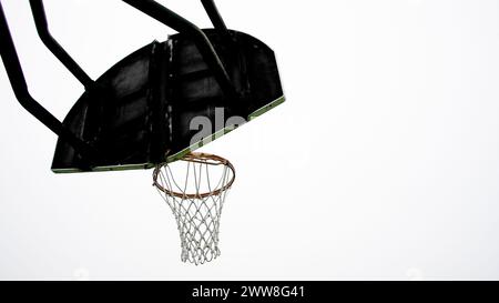 Un unico canestro da basket si erge alto con il bordo arancione, adagiato contro un cielo limpido e pallido, in attesa che i giocatori inizino una partita. Foto Stock