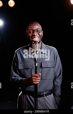 Ritratto verticale di un uomo afroamericano sorridente che parla al microfono sul palco esibendosi in uno spettacolo comico Foto Stock