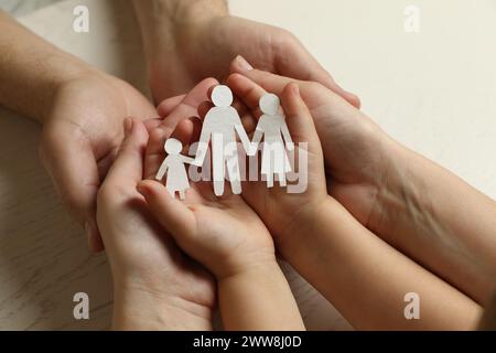 I genitori e i bambini hanno in mano un ritaglio di carta di famiglia al tavolo di legno bianco, primo piano Foto Stock