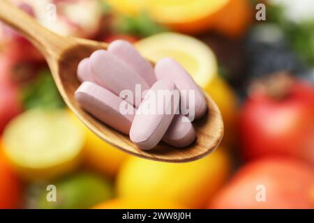 Pillole vitaminiche in cucchiaio contro frutta fresca, primo piano Foto Stock