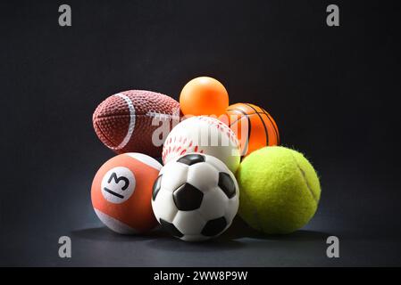 Vari concept sportivi con palle diverse su sfondo nero isolato. Vista frontale. Foto Stock