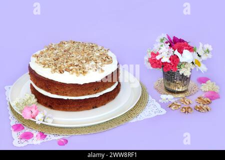 Torta ghiacciata di carote e noci con fiori estivi su sfondo viola. Delizioso concetto di cibo fatto in casa per il tè pomeridiano o la festa di compleanno. Foto Stock