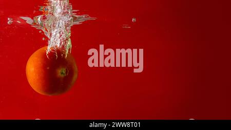 Pomodoro maturo cade profondamente sotto l'acqua con un grande splash. Foto Stock