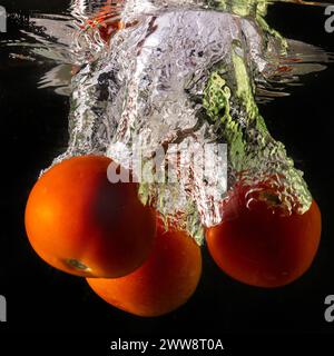 Pomodoro maturo cade profondamente sotto l'acqua con un grande splash. Foto Stock