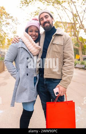 Coppia felice, sorriso ritratto e borse dello shopping in città insieme per moda, regalo o acquisto. Verticale Foto Stock