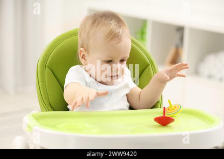 Giocattoli per bambini. Bambino carino che gioca con i top girevoli in seggiolone a casa Foto Stock