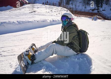 Snowboarder seduto sulla neve, concedendosi un momento di riposo su un pendio soleggiato. Foto Stock