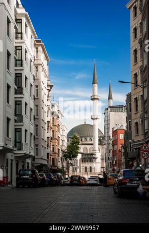 La nuova moschea in Piazza Taksim a Istanbul fotografata da una strada laterale piena di negozi e automobili Foto Stock