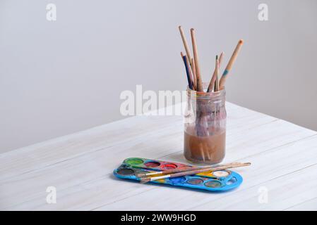 Barattolo con pennelli e acquerelli su tavolo in legno. Ideale per progetti creativi o temi artistici Foto Stock