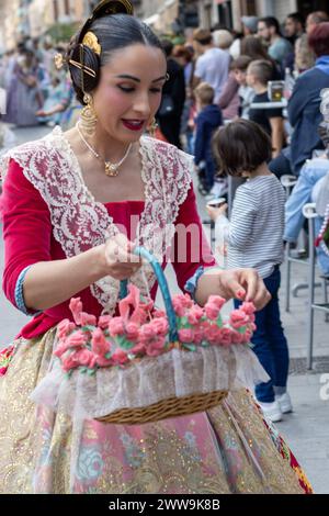 Vivaci celebrazioni al Fallas Festival di Gandia, Spagna. Un partecipante, adornato con un colorato abbigliamento tradizionale, tiene in mano un cestino di fiori, incarna Foto Stock