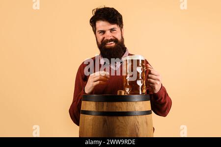 L'ora della birra. Uomo barbuto con tazza di birra su botte di legno. Sorridente bel maschio che beve birra. Tradizioni tedesche. Festival dell'Oktoberfest. Pub della birra e. Foto Stock