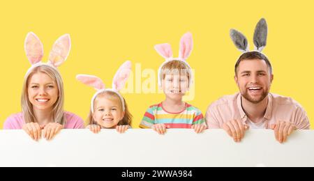 Famiglia felice con orecchie da coniglio e poster vuoto su sfondo giallo. Festa di Pasqua Foto Stock